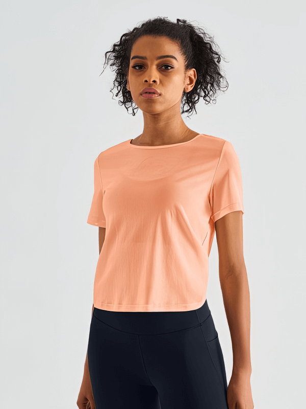 Model wearing stylish quick-drying women's open back T-shirt in solid peach, breathable nylon, perfect for workouts or casual wear.